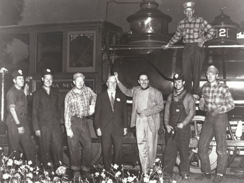 Photograph of eight men, including Walt Disney, standing in front of a train